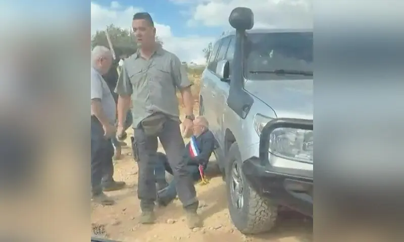 The mayor, wearing a blue, white and red sash, leans against a vehicle as masked men intercept and surround a car at a village in the occupied West Bank. —AFP