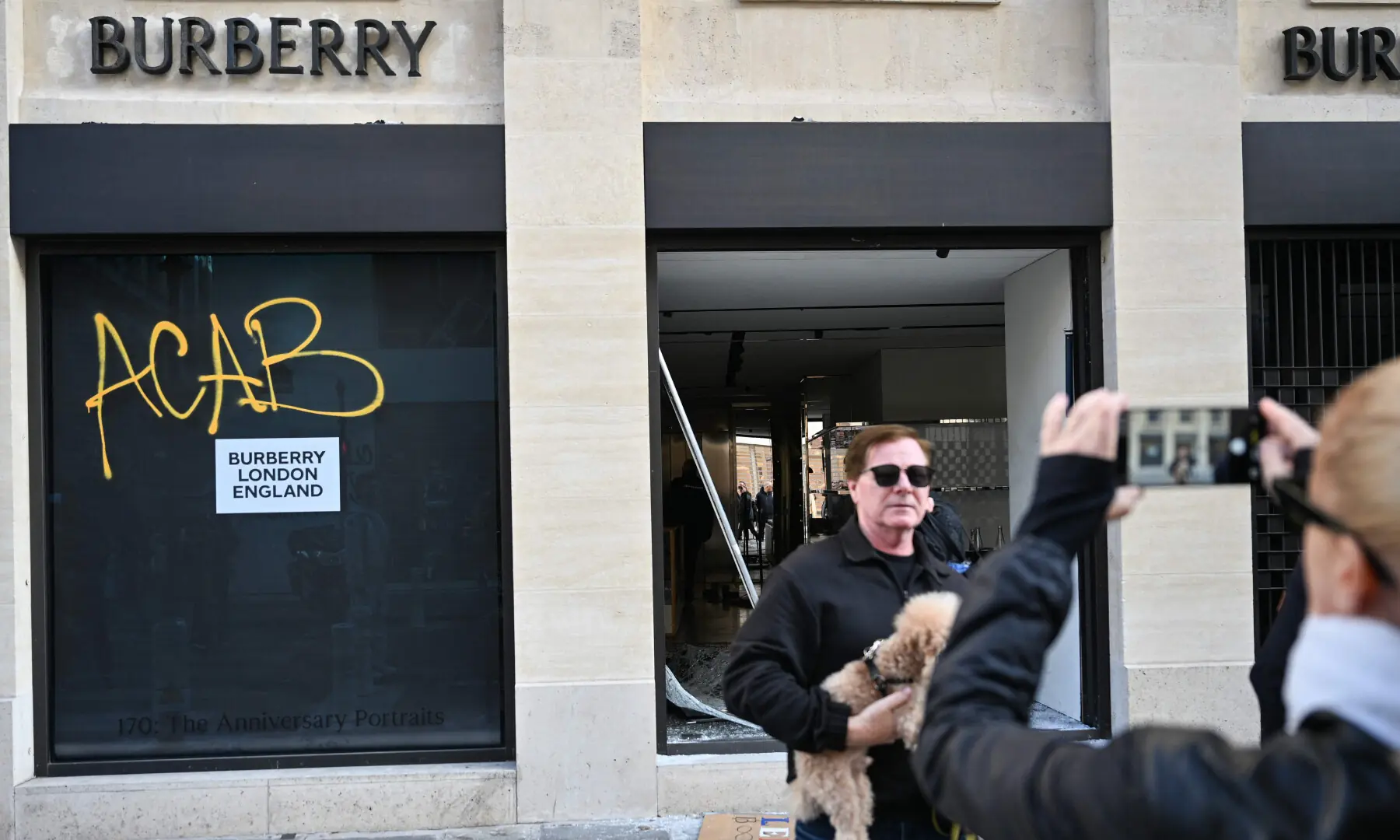  A pedestrian poses for pictures in front of a damaged &ldquo;Burberry&rdquo; shop reading the tag &ldquo;ACAB - All Cops Are Bastards&rdquo; in central Paris on Oct 18, 2026. &mdash; AFP 