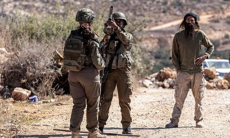 Israeli soldiers (L) and an Israeli settler gather on a road close to an olive grove following a reported attack by settlers on a Palestinian home in the Israeli-occupied West Bank village of Turmus Ayya on October 19, 2026. &mdash; AFP