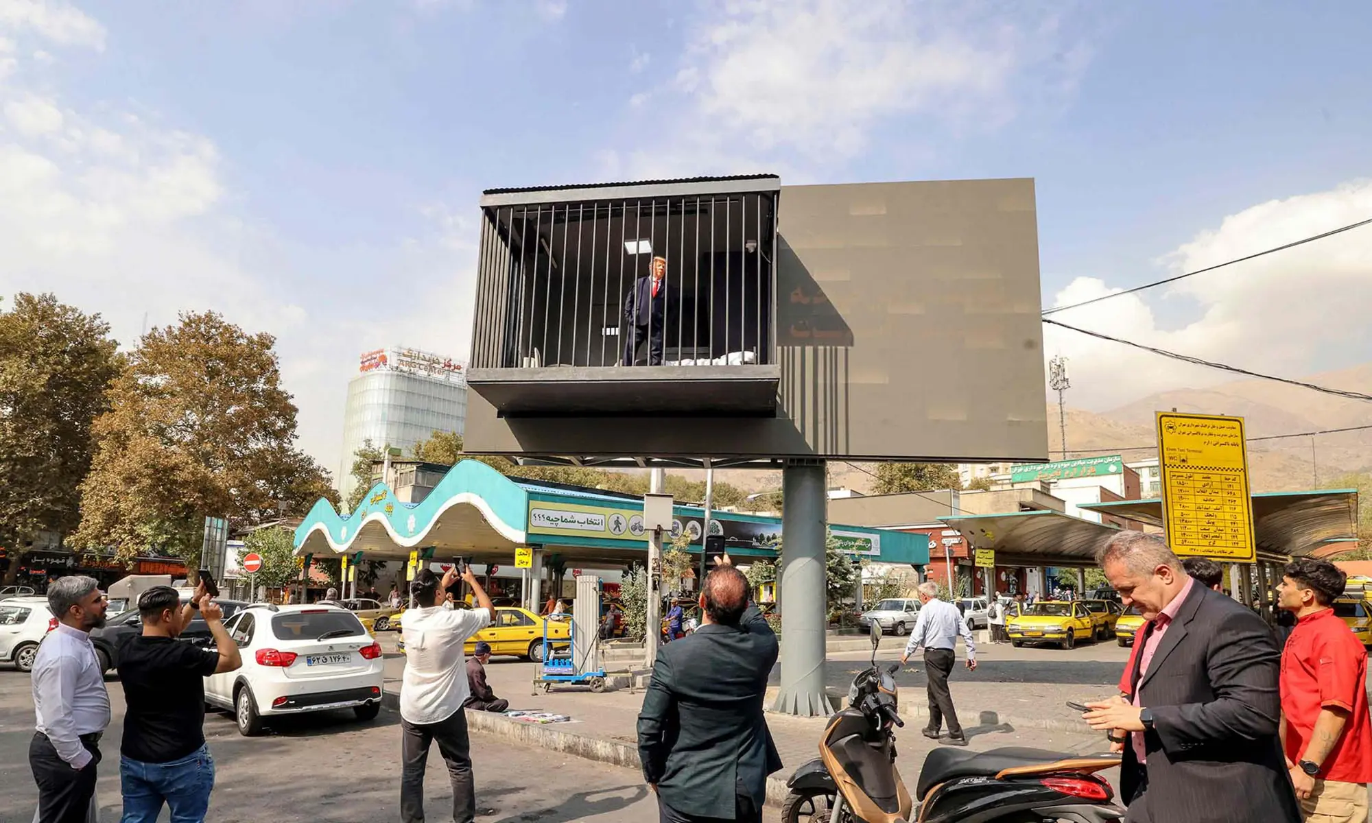 Pedestrians take pictures of an Iranian actor wearing a mask depicting US President Donald Trump as he poses inside a mock prison cell installed onto a street billboard at Tajrish Square in Tehran, Iran on October 21, 2026. — AFP