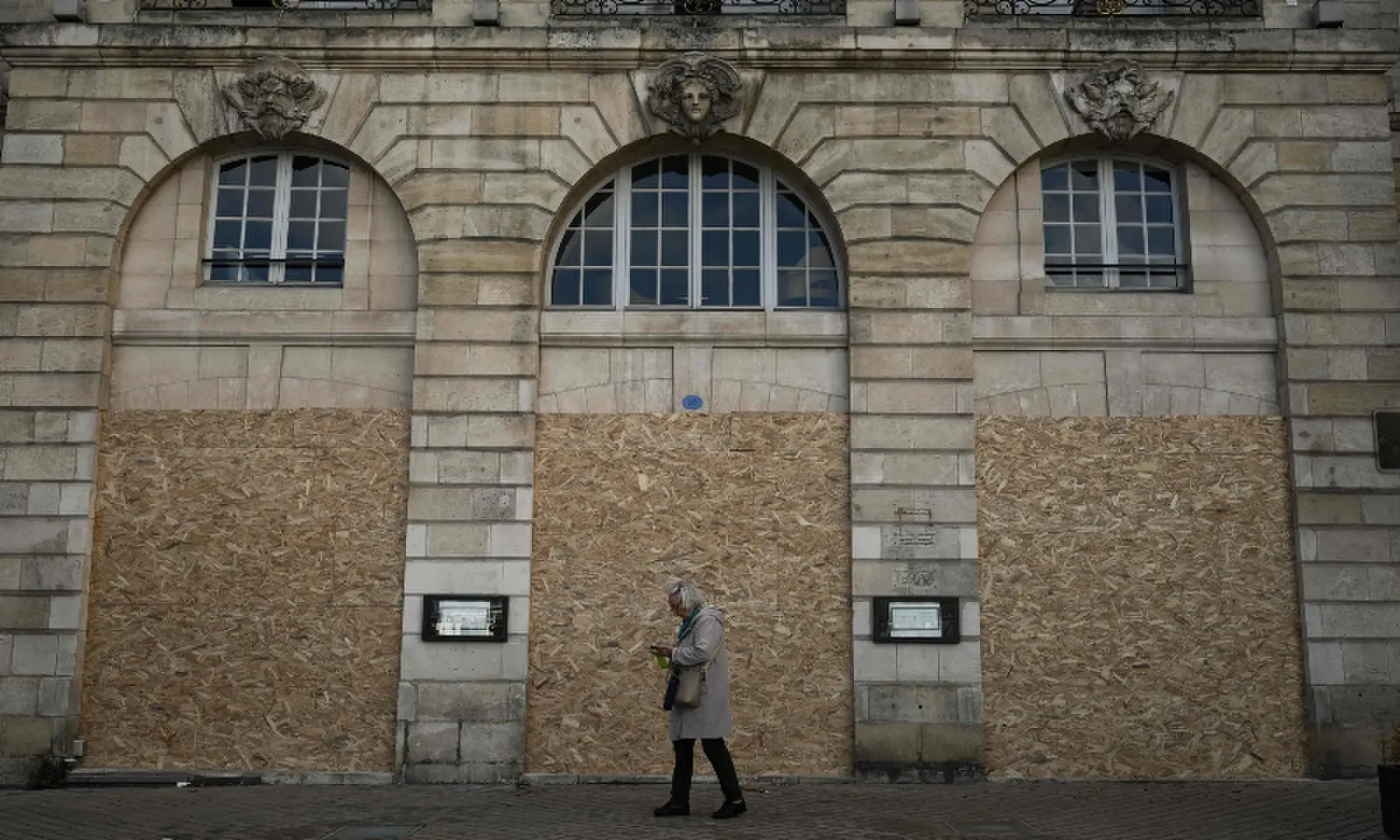 A woman walks past the boarded-up ground-floor windows of a historic building ahead of a demonstration planned for October 24, in central Bordeaux, southwestern France on October 23, 2026. — AFP